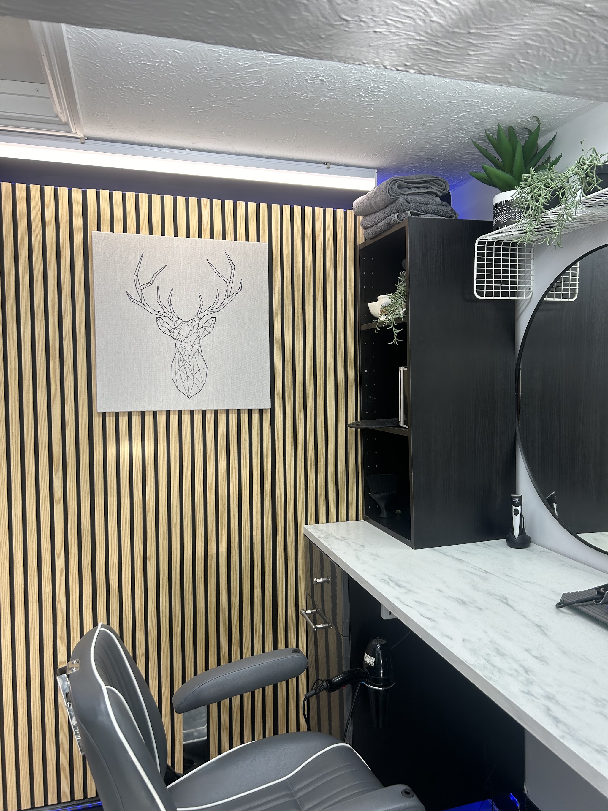Inside Sage’s Barbershop: a grey barber chair in front of an oak slatted wall with a stag line drawing