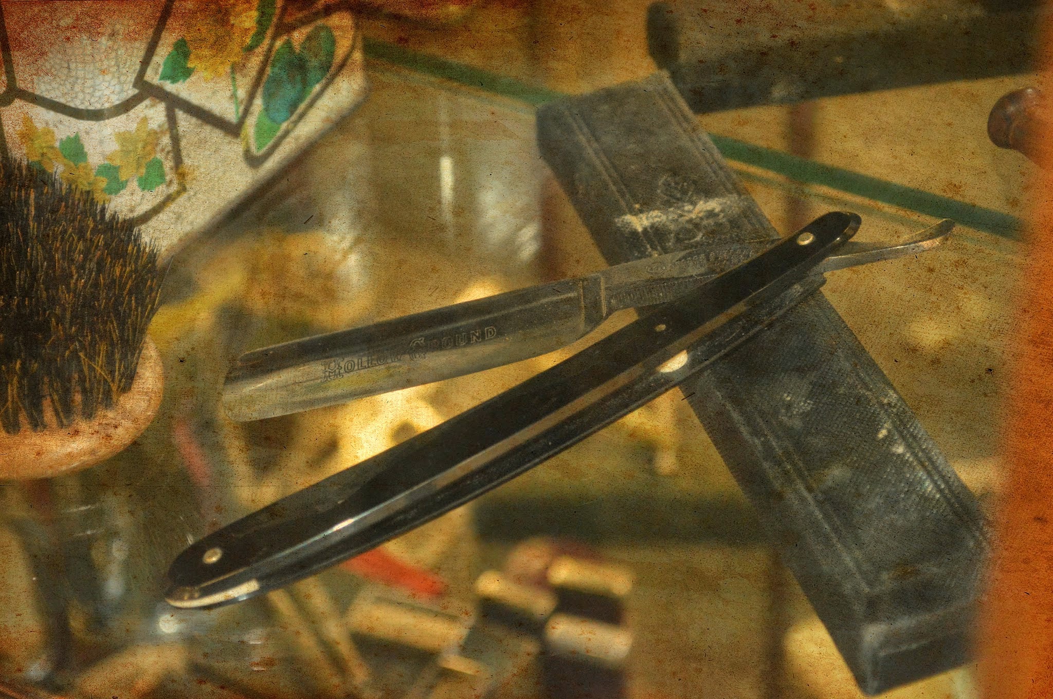 A straight razor, shaving brush and strop laid out on a glass counter